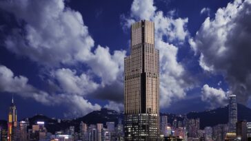 Vysoký mrakodrap v štýle art deco s vertikálne rebrovanou fasádou týčiaci sa nad hongkonským prístavom, obklopený nižšími budovami a horami pod dramatickou modrou oblohou s bielymi oblakmi.